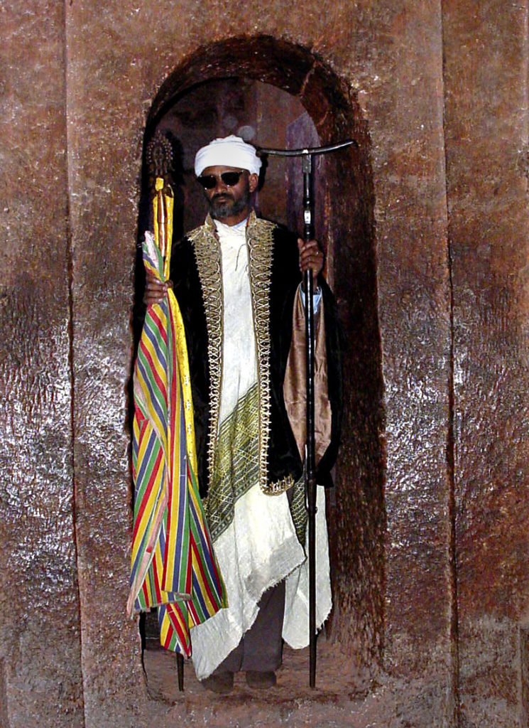 A Priest on duty in one of the cave churches in Lalibela. The churches are carved entirely out of one solid piece of stone set in the side of a mountain. This priest wore sunglasses to protect his eyes from the camera flash.